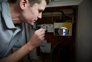 A man in front of a fuse box, holding a flashlight and inspecting the fuses during a power outage. He looks concerned as he tries to identify the source of the electrical issue. Keywords: power outage fix, fuse box inspection, electrical troubleshooting, electrician near me, emergency electrician, residential electrical repair, electrical service areas, electrical maintenance, electrical problems, home safety, Sacramento, Elk Grove, Roseville, Citrus Heights, Folsom, Rocklin.