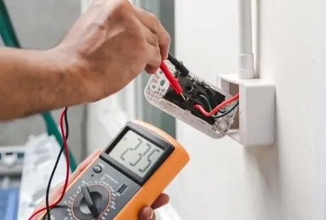 electrician testing wiring in wall outlet using digital multimeter during electrical repair